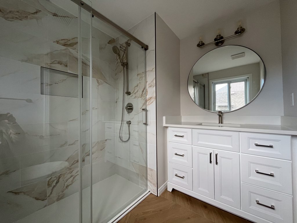 a bathroom with a glass shower and a round mirror